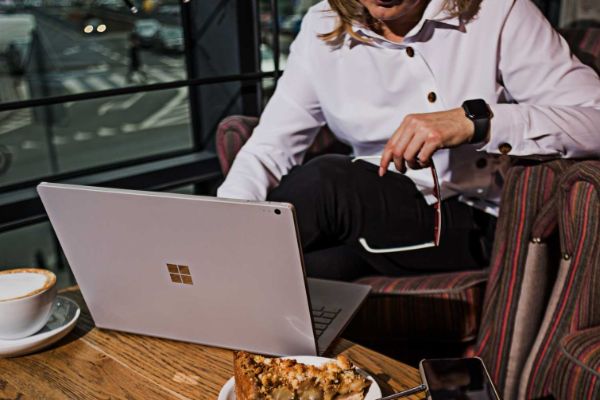Women in a coffee shop looking at a laptop with glasses in her hand